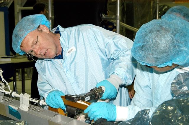 NASA image: KENNEDY SPACE CENTER, FLA. -  In the Space Station Processing Facility, STS-114 Mission Specialist Andrew Thomas (left) works with equipment while Mission Specialist Soichi Noguchi watches.  Noguchi is with the Japanese Aerospace Exploration Agency (JAXA).  They and other crew members are at KSC for equipment familiarization.  STS-114 is classified as Logistics Flight 1 to the International Space Station, delivering new supplies and replacing one of the orbital outpost’s Control Moment Gyroscopes (CMGs). STS-114 will also carry a Raffaello Multi-Purpose Logistics Module and the External Stowage Platform-2.  The crew is slated to conduct at least three spacewalks: They will demonstrate repair techniques of the Shuttle’s Thermal Protection System,  replace the failed CMG with one delivered by the Shuttle, and  install the External Stowage Platform.