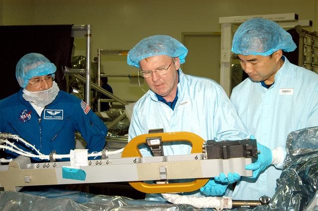 NASA image: KENNEDY SPACE CENTER, FLA. -  In the Space Station Processing Facility, STS-114 Mission Specialists Andrew Thomas (center) and Soichi Noguchi (right) work with equipment while Mission Specialist Charles Camarda (left) watches.  Noguchi is with the Japanese Aerospace Exploration Agency (JAXA).  They and other crew members are at KSC for equipment familiarization.  STS-114 is classified as Logistics Flight 1 to the International Space Station, delivering new supplies and replacing one of the orbital outpost’s Control Moment Gyroscopes (CMGs). STS-114 will also carry a Raffaello Multi-Purpose Logistics Module and the External Stowage Platform-2.  The crew is slated to conduct at least three spacewalks: They will demonstrate repair techniques of the Shuttle’s Thermal Protection System,  replace the failed CMG with one delivered by the Shuttle, and  install the External Stowage Platform.
