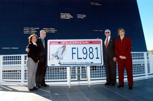 NASA image: KENNEDY SPACE CENTER, FLA. -  The new Florida license plate honoring the fallen astronauts of Challenger and Columbia is unveiled at the KSC Visitor Complex, in front of the Space Memorial Mirror.  Participants in the dedication included (from left) Susan Berry, a teacher from Mila Elementary School in Brevard County; Sen. Bill Posey; Florida Rep. Ralph Poppell; and Kirstie McCool Chadwick, sister of William “Willie” J. McCool, who was the pilot on mission STS-107 that ended in disaster Feb. 1, 2003.   The Space Mirror, 42-1/2 feet high by 50 feet wide, illuminates the names of the fallen astronauts cut through the monument’s black granite surface.