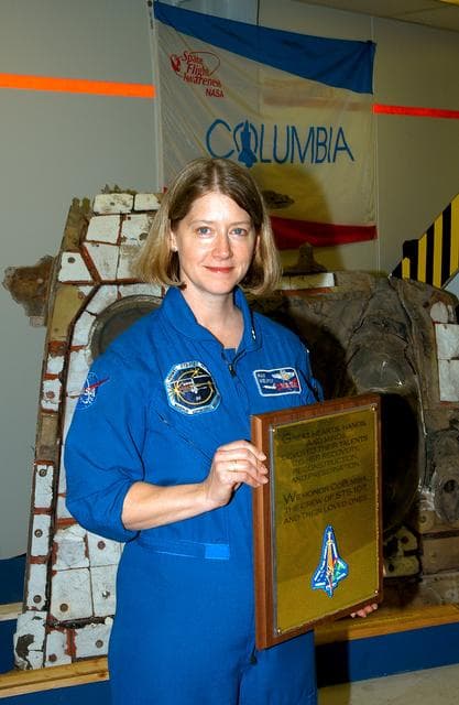 NASA image: KENNEDY SPACE CENTER, FLA. -  Posing with the plaque dedicated to Columbia Jan. 29, 2004,  is astronaut Pam Melroy.  The dedication ceremony included the 40-member preservation team gathered in the “Columbia room,” in the Vehicle Assembly Building.  The site is a permanent repository of the debris collected in the aftermath of the tragic accident Feb. 1, 2003, that claimed the orbiter and lives of the seven-member crew. Behind Melroy is a piece of the debris.