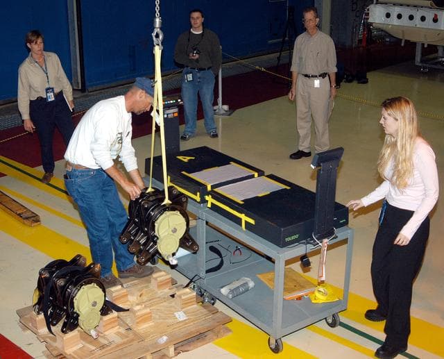 NASA image: KENNEDY SPACE CENTER, FLA. -  Workers in the Orbiter Processing Facility stand by while another guides the lifting of one of two rudder speed brake actuators onto a table to measure the alignment of its bearings.  The actuators move an orbiter’s rudder, speed brake, elevons and main engines during flight.
