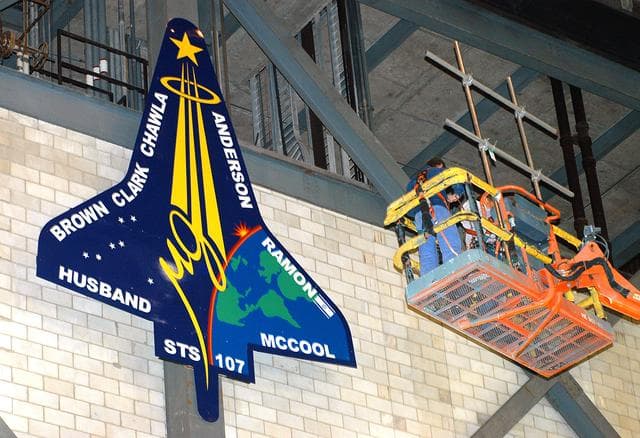 NASA image: KENNEDY SPACE CENTER, FLA. -  Workers install a 20-foot by 15-foot replica of the STS-107 logo above the “A” on the A tower in the transfer aisle of the Vehicle Assembly Building.  The debris from the orbiter Columbia, lost in a tragic accident on its return to Earth from the STS-107 mission, is permanently stored in the tower.  A dedication ceremony Jan. 29, 2004, revealed a plaque being installed in the storage area in honor of “Columbia, the crew of STS-107, and their loved ones.”