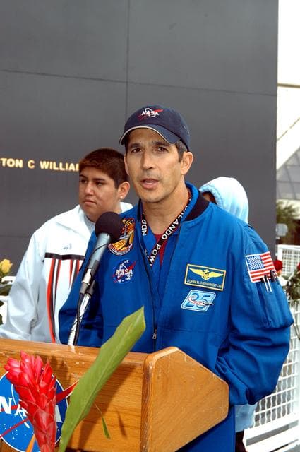 NASA image: KENNEDY SPACE CENTER, FLA. - Astronaut John Herrington speaks to the visitors at the memorial service held at the Space Memorial Mirror for the crew of Columbia.  Herrington, who is a Chickasaw from Oklahoma, introduced the Shoshone-Bannock Junior-Senior High School dancers, from the Native American community at Fort Hall, Idaho, who performed a healing ceremony.  Students and staff of the Shoshone-Bannock Nation had an experiment on board Columbia. Feb. 1 is the one-year anniversary of the loss of the crew and orbiter Columbia in a tragic accident as the ship returned to Earth following mission STS-107. The public was invited to the memorial service, held in the KSC Visitor Complex, which included comments by Center Director Jim Kennedy and Executive Director of Florida Space Authority Winston Scott.  Scott is a former astronaut who flew on Columbia in 1997.