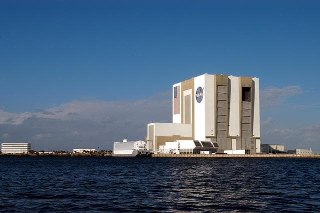 NASA image: KENNEDY SPACE CENTER, FLA. - From a boat on the Banana River the Vehicle Assembly Building looms over the water.  The boat holds Karen Holloway-Adkins, KSC wildlife specialist, who is studying the life history of sea turtles, especially what they eat, where they lay their eggs and what factors might harm their survival.  On the boat trip she is also monitoring the growth of sea grasses and algae and the water quality of estuaries and lagoons used by sea turtles and other aquatic wildlife.