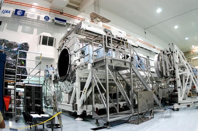 NASA image: KENNEDY SPACE CENTER, FLA. - Workers in the Space Station Processing Facility prepare to release the overhead crane from the Multi-Purpose Logistics Module Raffaello now secure on a new work stand.  Raffaello is the second MPLM built by the Italian Space Agency, serving as a reusable logistics carrier and primary delivery system to resupply and return station cargo requiring a pressurized environment.  It has been moved to allow the third MPLM, Donatello, to be brought in for routine testing.  Donatello has been stored in the Operations and Checkout Building.  This is the first time all three MPLMs are in the SSPF; the other one is the Leonardo.  Raffaello is scheduled to fly on Space Shuttle Atlantis on mission STS-114.