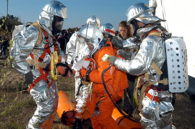 NASA image: KENNEDY SPACE CENTER, FLA. - Emergency crew members help a volunteer “astronaut” onto the ground after being lowered from the top of the orbiter crew compartment mock-up that is the scene of a “Mode VII” emergency landing simulation at Kennedy Space Center.  The purpose of the Mode VII is to exercise emergency preparedness personnel, equipment and facilities in rescuing astronauts from a downed orbiter and providing immediate medical attention.  This simulation presents an orbiter that has crashed short of the Shuttle Landing Facility in a wooded area 2-1/2 miles south of Runway 33.  Emergency crews are responding to the volunteer astronauts who are simulating various injuries.  Rescuers must remove the crew, provide triage and transport to hospitals those who need further treatment.  Local hospitals are participating in the exercise.