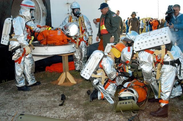 NASA image: KENNEDY SPACE CENTER, FLA. - Emergency crew members help an “injured” astronaut from the orbiter crew compartment mock-up during a “Mode VII” emergency landing simulation at Kennedy Space Center.  Another is on the ground.  The purpose of the Mode VII is to exercise emergency preparedness personnel, equipment and facilities in rescuing astronauts from a downed orbiter and providing immediate medical attention.  This simulation presents an orbiter that has crashed short of the Shuttle Landing Facility in a wooded area 2-1/2 miles south of Runway 33.  Emergency crews are responding to the volunteer astronauts who are simulating various injuries.  Rescuers must remove the crew, provide triage and transport to hospitals those who need further treatment.  Local hospitals are participating in the exercise.