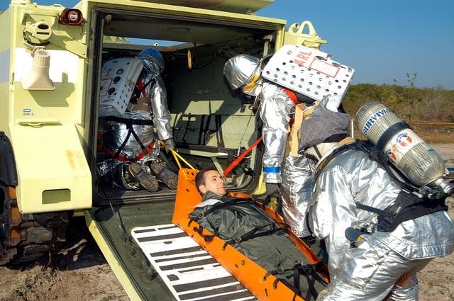 NASA image: KENNEDY SPACE CENTER, FLA. - An “injured” rescue worker is lifted into an M-113 armored personnel carrier provided for transportation during a “Mode VII” emergency landing simulation at Kennedy Space Center.  The purpose of the Mode VII is to exercise emergency preparedness personnel, equipment and facilities in rescuing astronauts from a downed orbiter and providing immediate medical attention.  This simulation presents an orbiter that has crashed short of the Shuttle Landing Facility in a wooded area 2-1/2 miles south of Runway 33.  Emergency crews are responding to the volunteer astronauts who are simulating various injuries inside the crew compartment mock-up.  Rescuers must remove the crew, provide triage and transport to hospitals those who need further treatment.  Local hospitals are participating in the exercise.