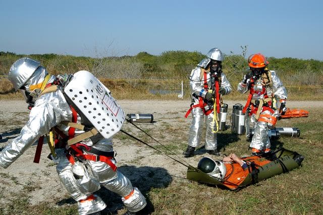 NASA image: KENNEDY SPACE CENTER, FLA. - Emergency crew members transport an “injured”  astronaut during a “Mode VII” emergency landing simulation at Kennedy Space Center.  The purpose of the Mode VII is to exercise emergency preparedness personnel, equipment and facilities in rescuing astronauts from a downed orbiter and providing immediate medical attention.  This simulation presents an orbiter that has crashed short of the Shuttle Landing Facility in a wooded area 2-1/2 miles south of Runway 33.  Emergency crews are responding to the volunteer astronauts who are simulating various injuries inside the crew compartment mock-up.  Rescuers must remove the crew, provide triage and transport to hospitals those who need further treatment.  Local hospitals are participating in the exercise.