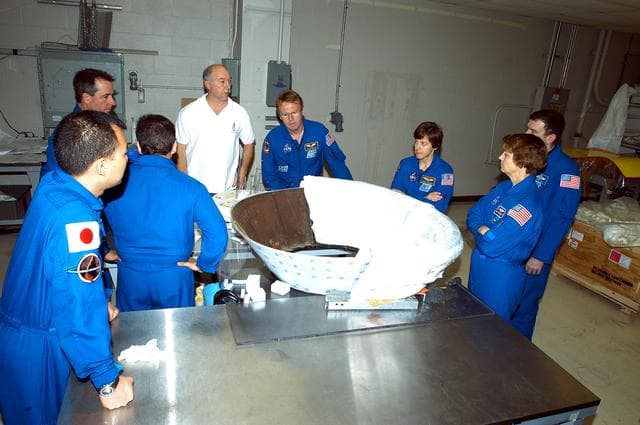 NASA image: KENNEDY SPACE CENTER, FLA. - Members of the STS-114 crew spend time becoming familiar with Shuttle and mission equipment. From left (in their blue suits) are Mission Specialists Soichi Noguchi, Stephen Robinson, Charles Camarda, Andrew Thomas and Wendy Lawrence; Commander Eileen Collins and Pilot James Kelly. Noguchi represents the Japanese Aerospace and Exploration Agency.   They are looking at the thermal protection system insulation blankets being installed on an insert for Discovery’s nose cap. The STS-114 mission is Logistics Flight 1, which is scheduled to deliver supplies and equipment plus the external stowage platform to the International Space Station.