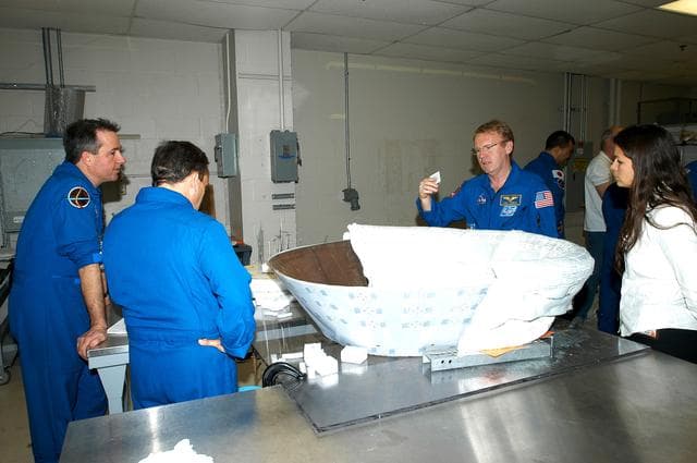 NASA image: KENNEDY SPACE CENTER, FLA. - Members of the STS-114 crew spend time becoming familiar with Shuttle and mission equipment.  From left are Mission Specialists Stephen Robinson, Charles Camarda and Andrew Thomas.  On the work stand is the insert for Discovery’s nose cap, which is being fitted with themal protection system insulation blankets.  The mission is Logistics Flight 1, which is scheduled to deliver supplies and equipment plus the external stowage platform to the International Space Station.