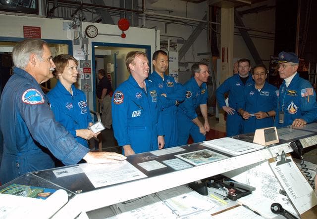 NASA image: KENNEDY SPACE CENTER, FLA. - The STS-114 crew stands in front of the operations desk in the Orbiter Processing Facility.  At far right is astronaut John Young, who flew on the first flight of Space Shuttle Columbia with Robert Crippen. Young is associate director, Technical, at Johnson Space Center.  From left are Young’s pilot; STS-114 Commander Eileen Collins; Mission Specialists Andrew Thomas, Soichi Noguchi and Stephen Robinson; Pilot James Kelly; and Mission Specialist Charles Camarda. Noguchi represents the Japanese Aerospace and Exploration Agency.  The STS-114 crew is spending time becoming familiar with Shuttle and mission equipment.  The mission is Logistics Flight 1, which is scheduled to deliver supplies and equipment plus the external stowage platform to the International Space Station.