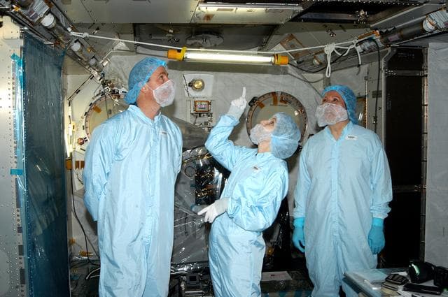 NASA image: KENNEDY SPACE CENTER, FLA. - In the Space Station Processing Facility, STS-114 Mission Specialist Stephen Robinson (left) looks at an area overhead in the Japanese Experiment Module (JEM). In the center is Jennifer Goldsmith, with United Space Alliance at Johnson Space Center, and at right is Louise Kleba, with USA at KSC.  Crew members are at KSC becoming familiar with Shuttle and mission equipment. The mission is Logistics Flight 1, which is scheduled to deliver supplies and equipment plus the external stowage platform to the International Space Station.