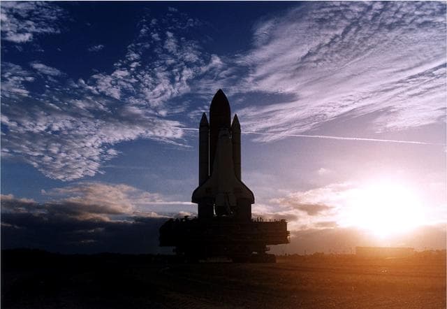 NASA image: KENNEDY SPACE CENTER, FLA. -  The rising sun and some scattered clouds provide a picturesque backdrop for the Space Shuttle Discovery as it travels along the crawlerway toward Launch Pad 39A in preparation for the STS-82 mission.  The Shuttle is on a Mobile Launcher Platform, and the entire assemblage is being carried by a large, tracked vehicle called the crawler transporter.  A seven-member crew will perform the second servicing of the orbiting Hubble Space Telescope (HST) during the 10-day STS-82 flight, whcih is targeted for a Feb. 11 liftoff.