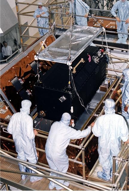 NASA image: KENNEDY SPACE CENTER, FLA. - Workers in KSC's Vertical Processing Facility lower the Near Infrared Camera and Multi-Object Spectrometer (NICMOS) into the Second Axial Carrier.  NICMOS is one of two new scientific instruments that will replace two outdated instruments on the Hubble Space Telescope (HST).  NICMOS will provide HST with the capability for infrared imaging and spectroscopic observations of astronomical targets.  The refrigerator-sized NICMOS also is HST's first cryogenic instrument — its sensitive infrared detectors must operate at very cold temperatures of minus 355 degrees Fahrenheit or 58 degrees Kelvin.  NICMOS will be installed in Hubble during STS-82, the second Hubble Space Telescope servicing mission.  Liftoff is targeted Feb. 11 aboard Discovery with a crew of seven.