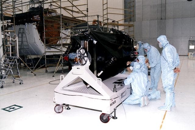NASA image: KENNEDY SPACE CENTER, FLA. - Workers in KSC's Vertical Processing Facility inspect the Near Infrared Camera and Multi-Object Spectrometer (NICMOS) on its handling fixture.  NICMOS is one of two new scientific instruments that will replace two outdated instruments on the Hubble Space Telescope (HST).  NICMOS will provide HST with the capability for infrared imaging and spectroscopic observations of astronomical targets.  The refrigerator-sized NICMOS also is HST's first cryogenic instrument — its sensitive infrared detectors must operate at very cold temperatures of minus 355 degrees Fahrenheit or 58 degrees Kelvin.  NICMOS will be installed in Hubble during STS-82, the second Hubble Space Telescope servicing mission.  Liftoff is targeted Feb. 11 aboard Discovery with a crew of seven.