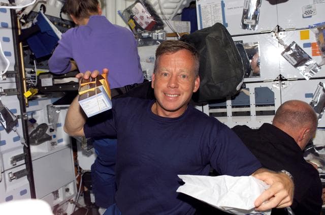 NASA image: Linsdey holds up boxes of chocolate covered coffee beans in the MDK during STS-121