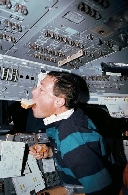 NASA image: STS-43 Pilot Baker eats a sandwich on OV-104's forward flight deck