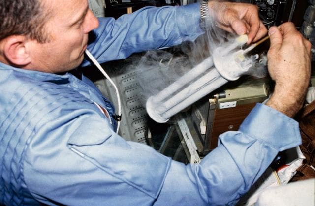 NASA image: Commander Lousma works with EEVT experiment and cryogenic tube on aft middeck