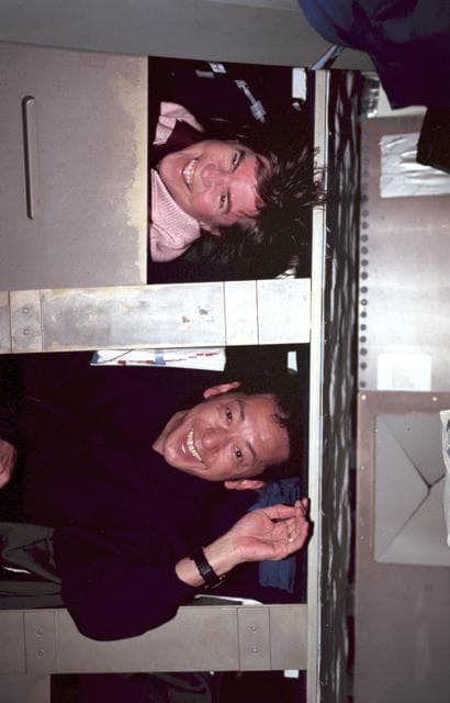 NASA image: STS-99 MS Voss and MS Mohri pose in sleep stations on OV-105's middeck