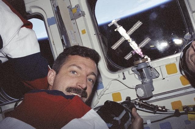 NASA image: MS Burbank poses at a window showing the ISS during STS-106