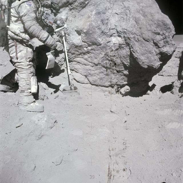 NASA image: Astronaut Charles Duke stands at rock adjacent to "House Rock"