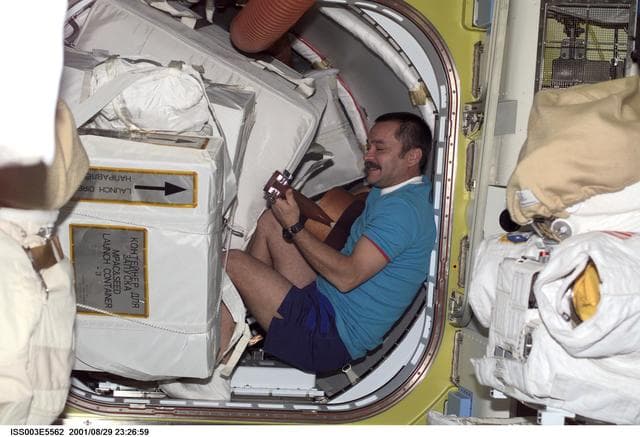 NASA image: Tyurin plays a guitar among stowage bags in the Airlock during Expedition Three
