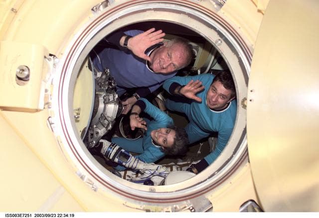 NASA image: The Soyuz Taxi crew wave through a Soyuz hatch during their visit to the ISS