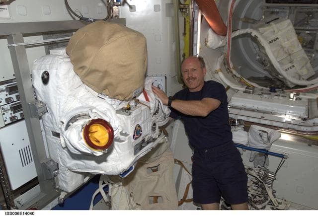 NASA image: Commander Kenneth D. Bowersox poses next to the torso portion of an EVA in the Quest Airlock