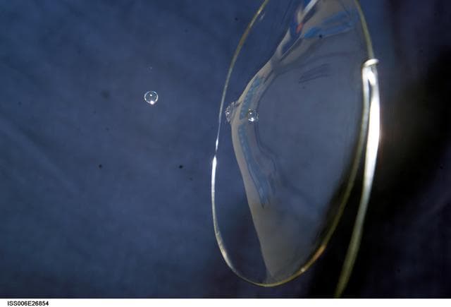NASA image: View of a surface tension demonstration using water that is being held in place by a 50mm metal loop