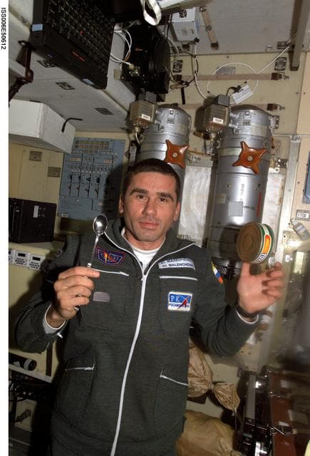 NASA image: Yuri I. Malenchenko is holding a spoon while a can of food floats nearby in the SM
