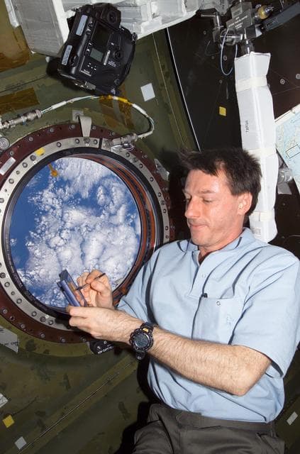 NASA image: Foale enters data on handheld palm pilot next to photo window in U.S. Lab during Expedition 8