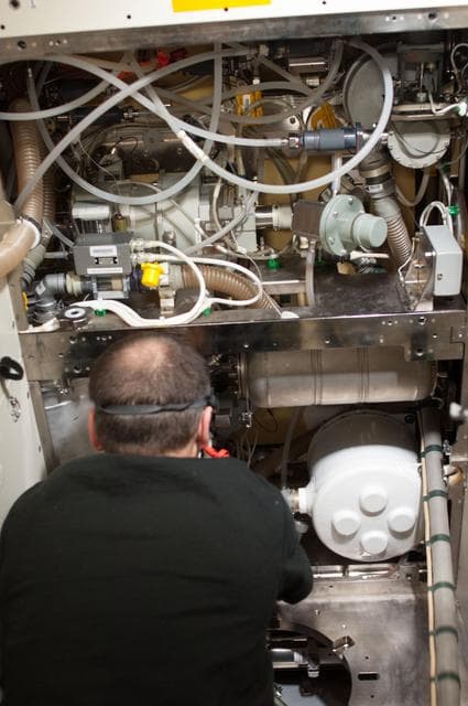 NASA image: Marshburn removing and replacing the WHC piping during routine maintenance