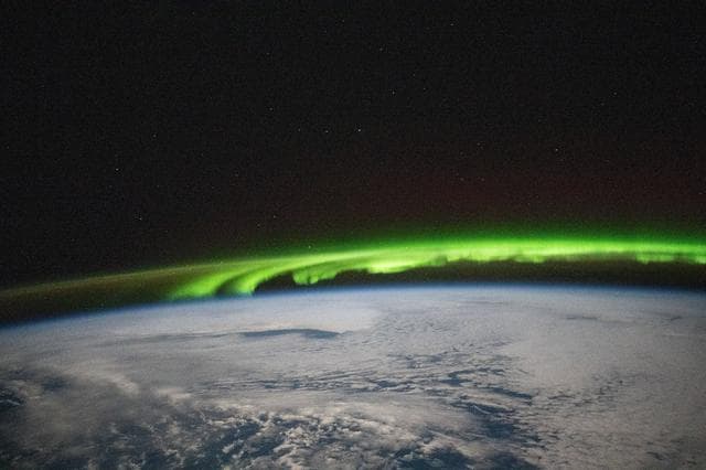 NASA image: A bright green aurora borealis streams above Earth's surface