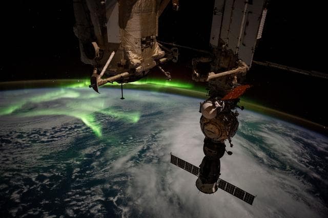 NASA image: The aurora australis arcs back and forth above a partly cloudy Indian Ocean