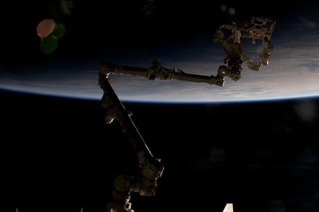 NASA image: The Canadarm2 is partially silhouetted against an orbital sunrise