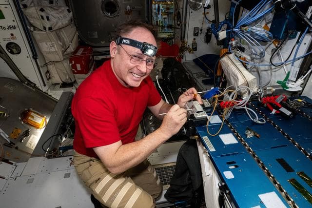 NASA image: NASA astronaut Mike Fincke replaces thermal tape on a spacesuit camera