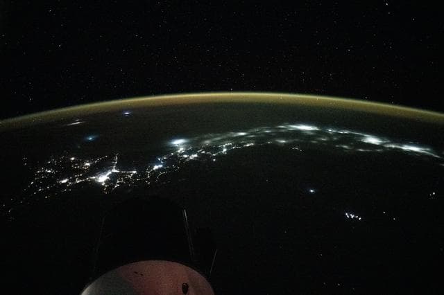 NASA image: City lights trace the Japanese coastline underneath a dim yellow-green airglow