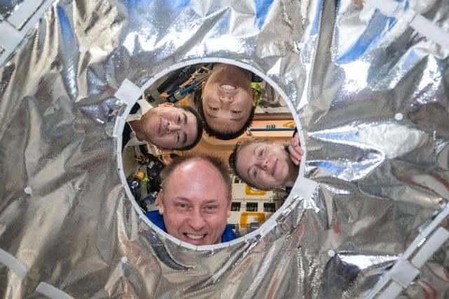 NASA image: Expedition 73 crewmates pose for a playful portrait through a hatch thermal cover 