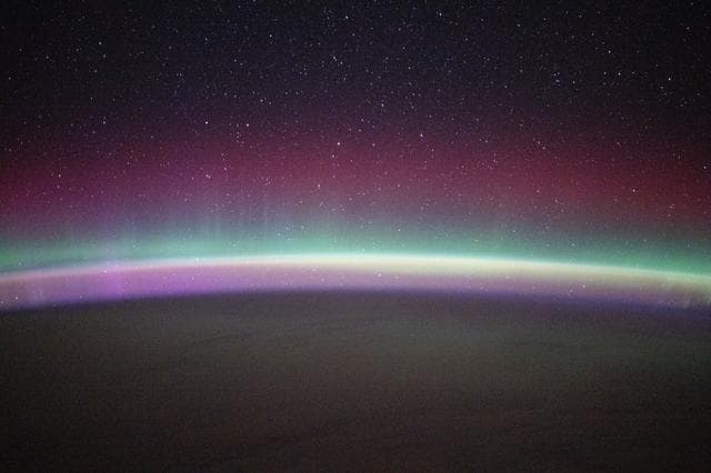 NASA image: A green and red aurora australis shimmers beneath a starry sky