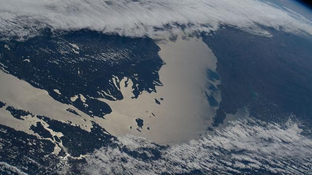 NASA image: Lake Michigan beams in the afternoon sunlight as clouds blanket its southern tip