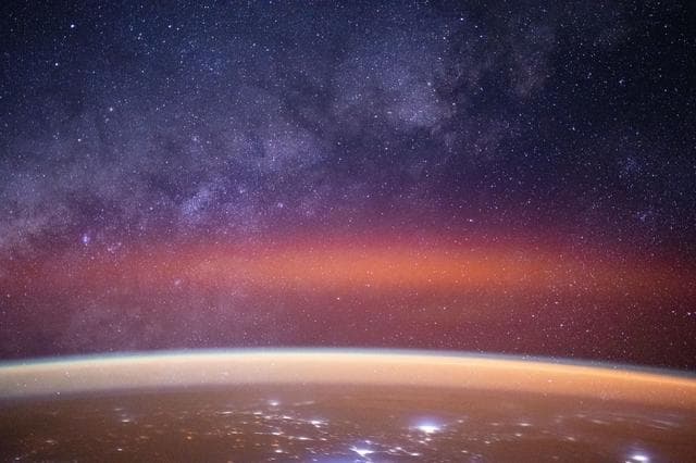 NASA image: The Milky Way spans the night sky above a bright orange-yellow airglow