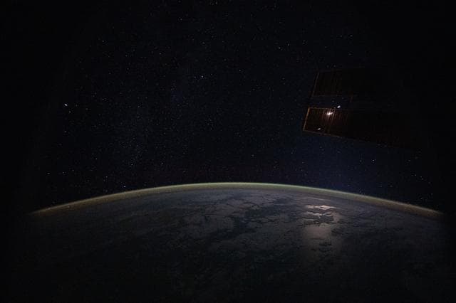 NASA image: A yellow‑green airglow blanketing Earth’s atmosphere beneath a starry sky