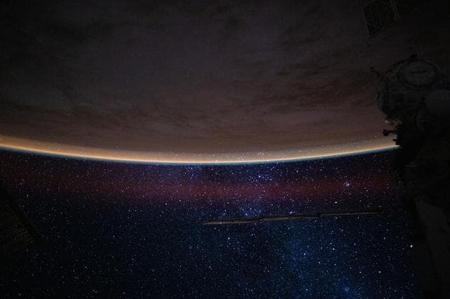 NASA image: A bright orange airglow outlines Earth’s horizon beneath the starry expanse of the night sky
