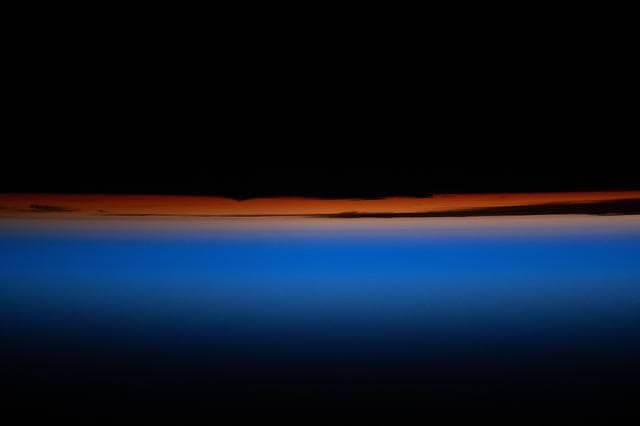 NASA image: A multi-hued orbital sunset revealing the tops of clouds fades above Earth's horizon