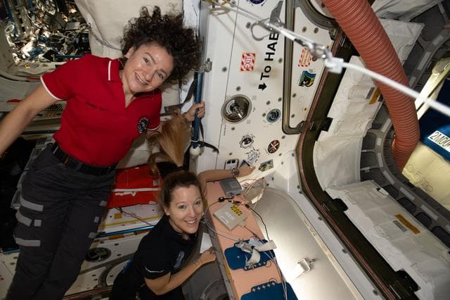 NASA image: Astronauts Jessica Meir and Sophie Adenot show off a Cygnus mission sticker