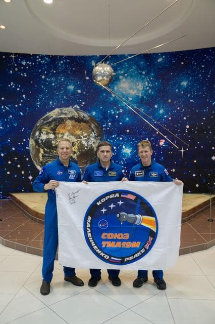 NASA image: During a break from training, the Expedition 46-47 crewmembers toured the Korolev Museum at the Baikonur Cosmodrome in Kazakhstan Dec. 10 and displayed a flag bearing the logo for their Soyuz mission. From left to right are Tim Kopra of NASA,  Yuri Malenchenko of the Russian Federal Space Agency (Roscosmos) and Tim Peake of the European Space Agency. Kopra, Peake and Malenchenko will launch Dec. 15 on the Soyuz TMA-19M spacecraft for a six-month mission on the International Space Station...NASA/Victor Zelentsov.