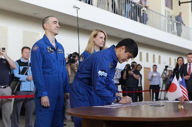 NASA image: At the Gagarin Cosmonaut Training Center in Star City, Russia, Expedition 48-49 prime crewmember Takuya Onishi of the Japan Aerospace Exploration Agency signs in for the start of final qualification exams May 26 as his crewmates, Anatoly Ivanishin of Roscosmos (left) and Kate Rubins of NASA (right) look on. Rubins, Onishi and Ivanishin will launch June 24 on the Soyuz MS-01 spacecraft from the Baikonur Cosmodrome in Kazakhstan for a four-month mission on the International Space Station...NASA/Stephanie Stoll.