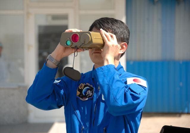 NASA image: Outside the Integration Facility at the Baikonur Cosmodrome in Kazakhstan, Expedition 48-49 crewmember Takuya Onishi of the Japan Aerospace Exploration Agency tries out a pair of binoculars June 25 as he prepares for launch July 7, Baikonur time, on the Soyuz MS-01 spacecraft with Kate Rubins of NASA and Anatoly Ivanishin of Roscosmos for a planned four-month mission on the International Space Station...NASA/Alexander Vysotsky.