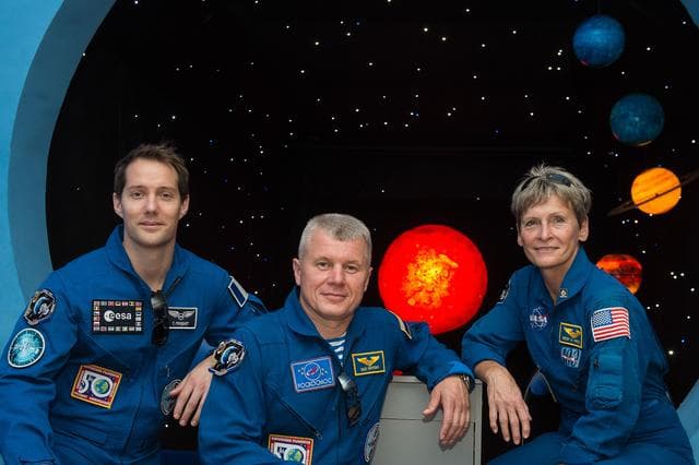 NASA image: During a tour of a museum in Baikonur, Kazakhstan June 26, Expedition 48-49 backup crewmembers Thomas Pesquet of the European Space Agency (left), Oleg Novitskiy of Roscosmos (center) and Peggy Whitson of NASA (right) pose for pictures in front of a mural depicting planets. Whitson, Novitskiy and Pesquet are backups to Kate Rubins of NASA, Anatoly Ivanishin of Roscosmos and Takuya Onishi of the Japan Aerospace Exploration Agency, who are preparing for launch on July 7, Baikonur time, on the Soyuz MS-01 spacecraft for a planned four-month mission on the International Space Station...GCTC/Andrei Shelepin.